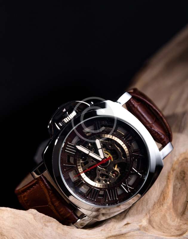 skeleton dial watch with a brown leather strap sitting on a piece of natural wood